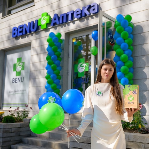 Млада жена пред аптека BENU държи балони и подаръчна торбичка